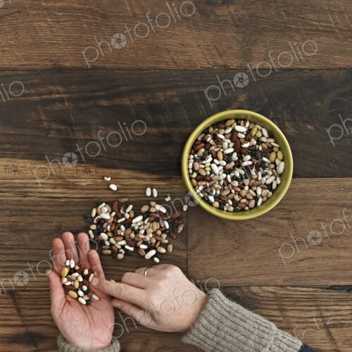 A person sorting different kinds of beans and pulses in her hands on a wooden table top. A person sorting different kinds of beans and pulses in her hands on a wooden table top.
