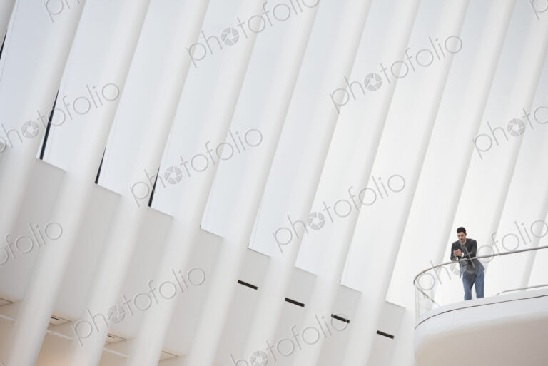 A person standing alone in an atrium by a railing, alone in a large space.