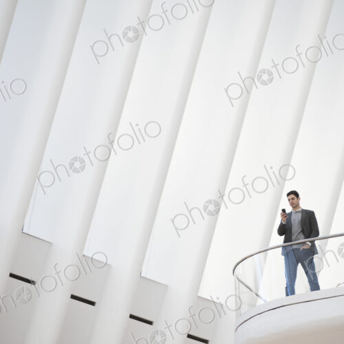 A person standing alone in an atrium by a railing on a balcony. A person standing alone in an atrium by a railing on a balcony.