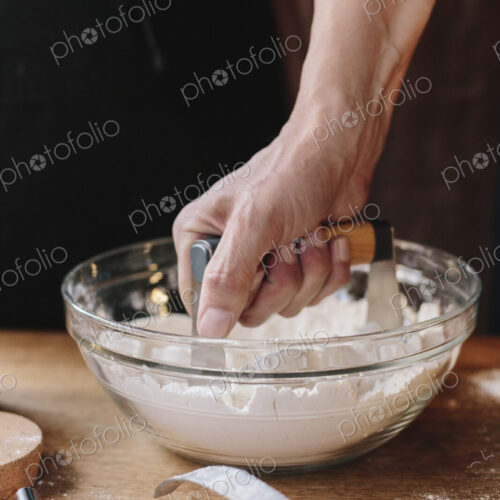 A person using a masher to soften butter in a bowl and mix pastry.