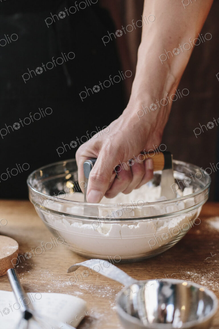 A person using a masher to soften butter in a bowl and mix pastry.