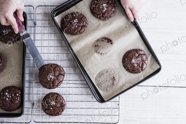 A person using a palette knife to move baked chocolate brownies from a baking tray to…