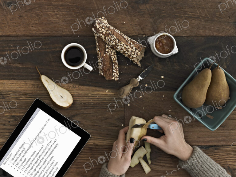 A person using a peeling knife to peel a pear. A computer tablet device with the…