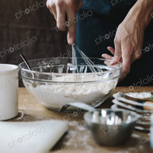 A person using a whisk to mix ingredients in a bowl, on a kitchen table. A person using a whisk to mix ingredients in a bowl, on a kitchen table.