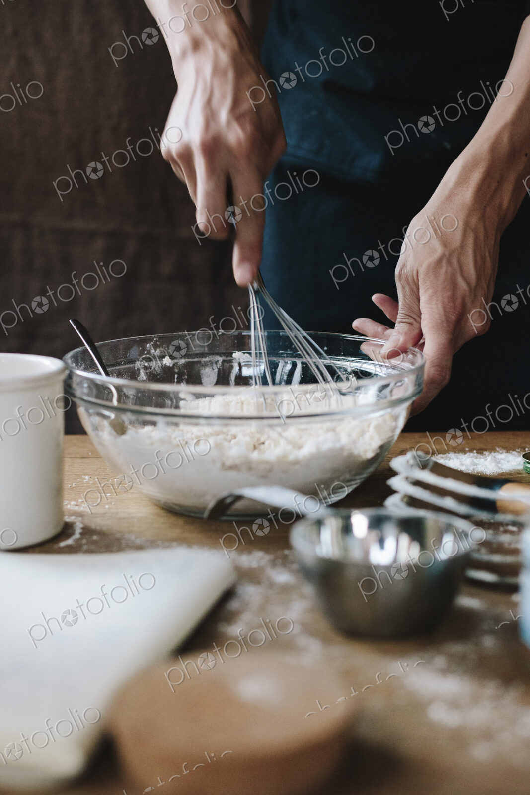 A person using a whisk to mix ingredients in a bowl, on a kitchen table.