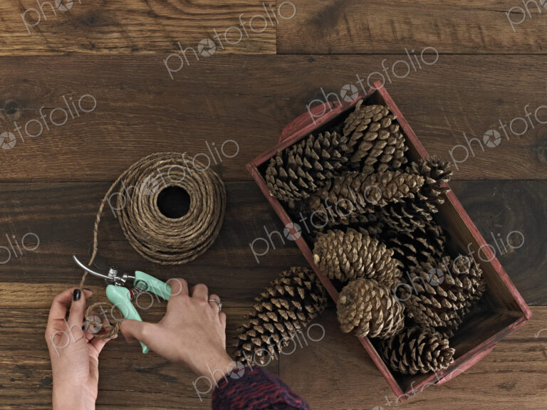 A person using secateurs or cutters on string. A box of pine cones.