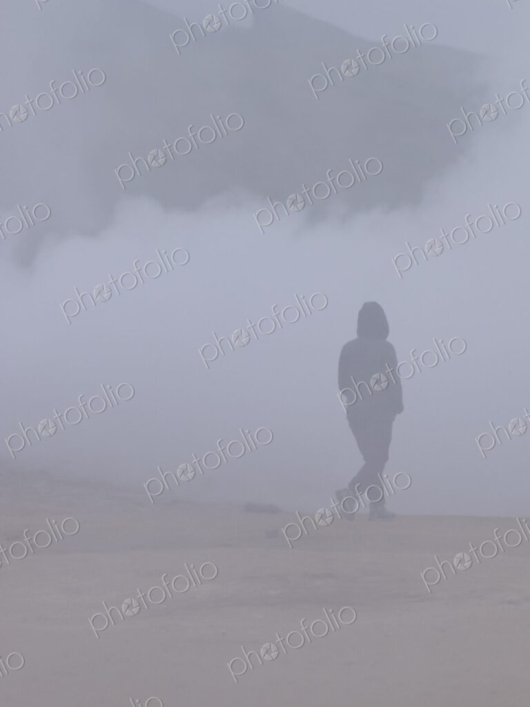 A person walking through the vapour and steam from the hot springs.