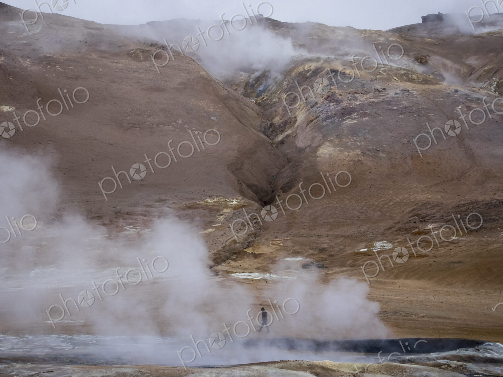 A person walks along the steamy edge of a hot spring.