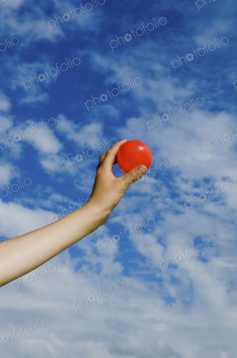 A person's outstretched hand, holding a red ball.