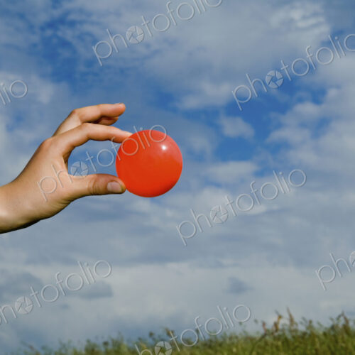 A person's outstretched hand, holding a red ball. A person's outstretched hand, holding a red ball.