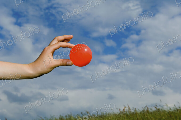 A person's outstretched hand, holding a red ball.