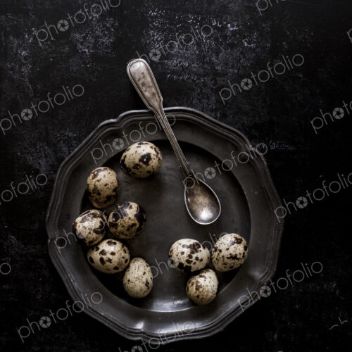 A pewter plate with small spotted quail's eggs and a spoon. A pewter plate with small spotted quail's eggs and a spoon.