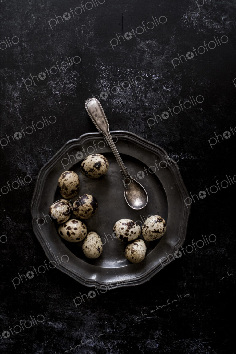 A pewter plate with small spotted quail's eggs and a spoon.
