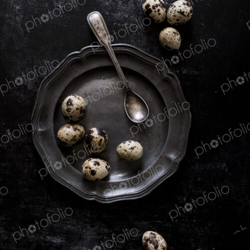 A pewter plate with small spotted quail's eggs and a spoon. A pewter plate with small spotted quail's eggs and a spoon.