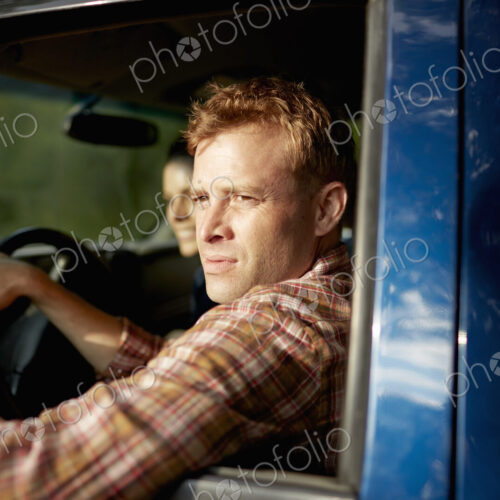 A pick up truck. A man at the wheel looking out of the window, with a young woman…