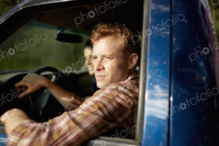 A pick up truck. A man at the wheel looking out of the window, with a young woman…