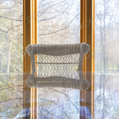 A picture window view to woodland, a glass table and white cane chair. A picture window view to woodland, a glass table and white cane chair.
