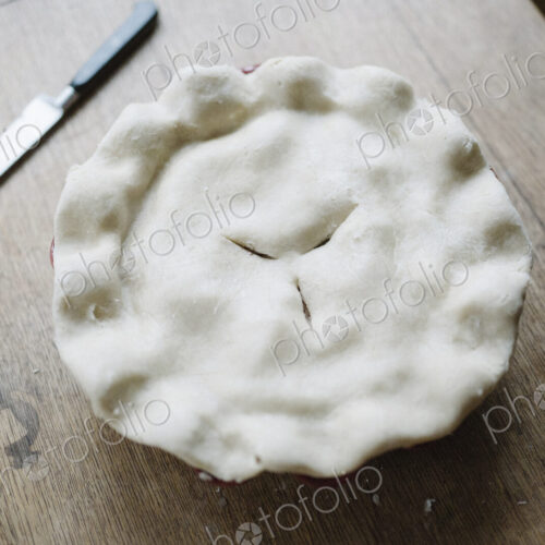 A pie with a home made uncooked pastry top and crimped edge. A pie with a home made uncooked pastry top and crimped edge.