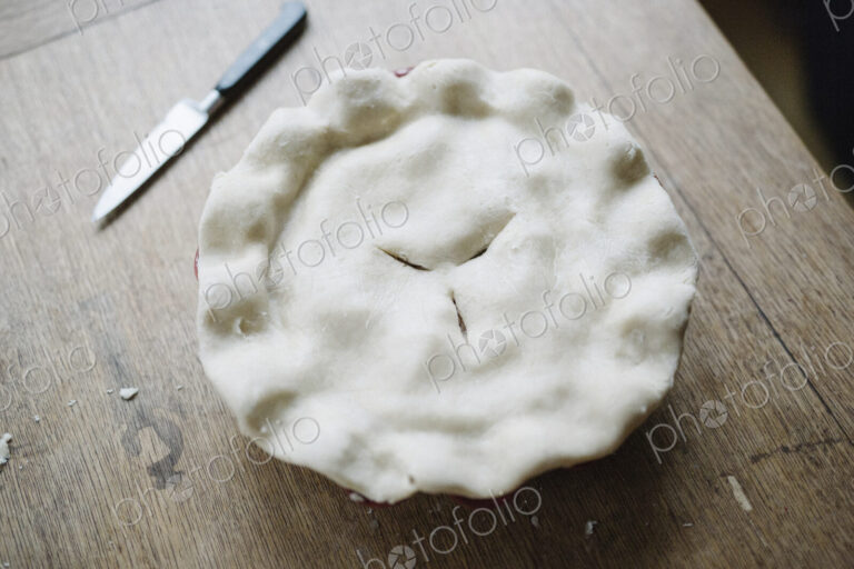 A pie with a home made uncooked pastry top and crimped edge.