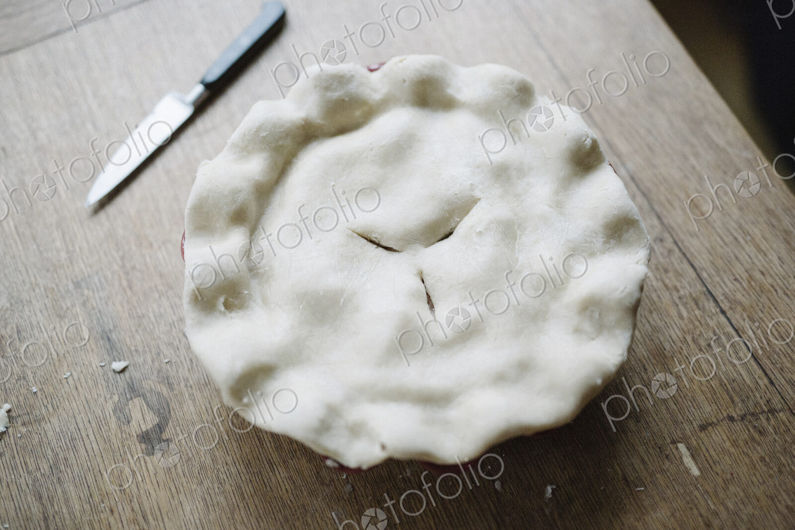 A pie with a home made uncooked pastry top and crimped edge.