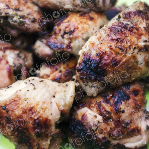 A plate of grilled barbequeued chicken pieces on a table outdoors. A plate of grilled barbequeued chicken pieces on a table outdoors.