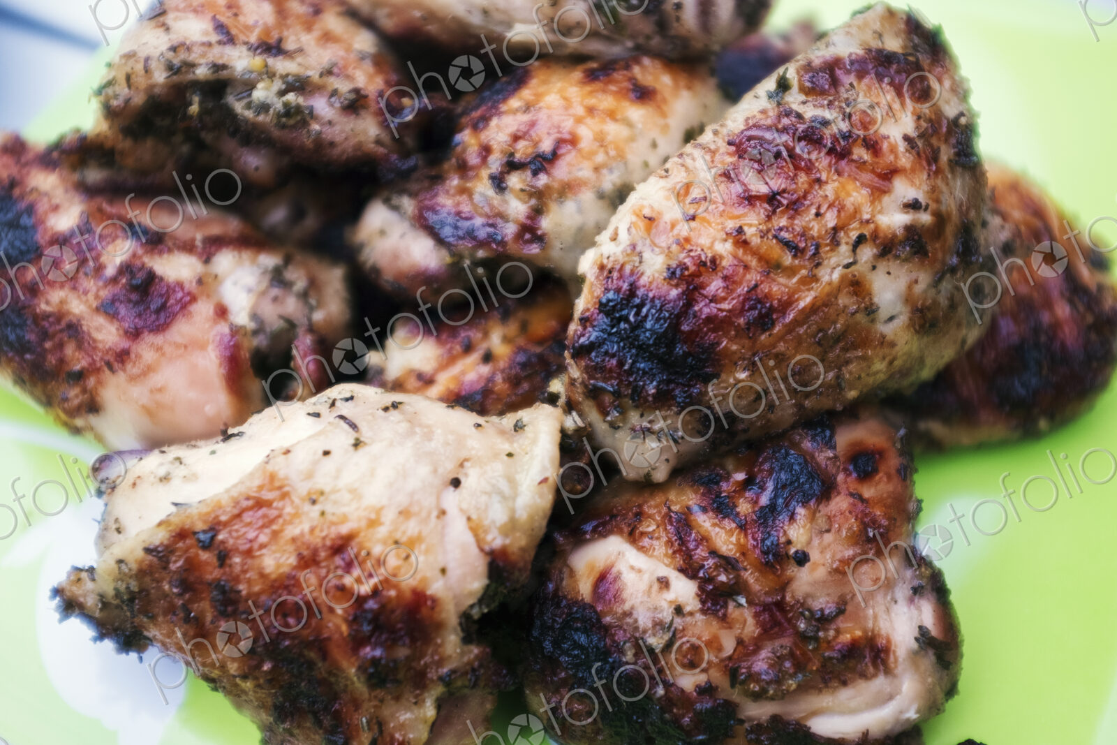 A plate of grilled barbequeued chicken pieces on a table outdoors.