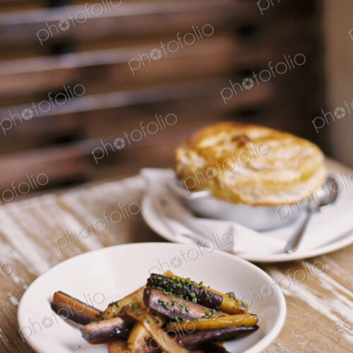 A plate of roasted vegetables cut into batons, and a pie on a tabletop. A plate of roasted vegetables cut into batons, and a pie on a tabletop.