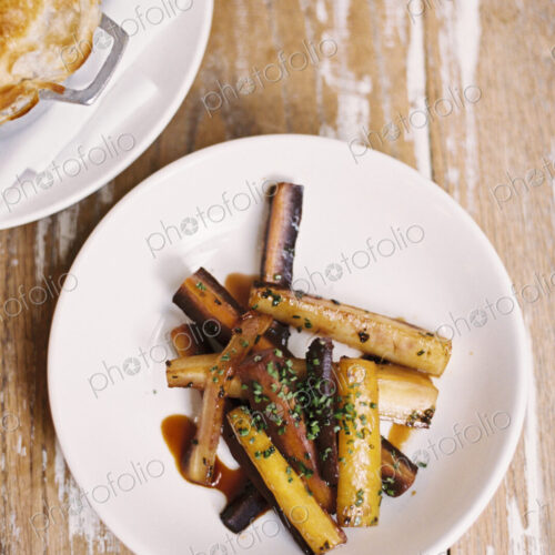 A plate of roasted vegetables cut into batons, and a pie on a tabletop. A plate of roasted vegetables cut into batons, and a pie on a tabletop.