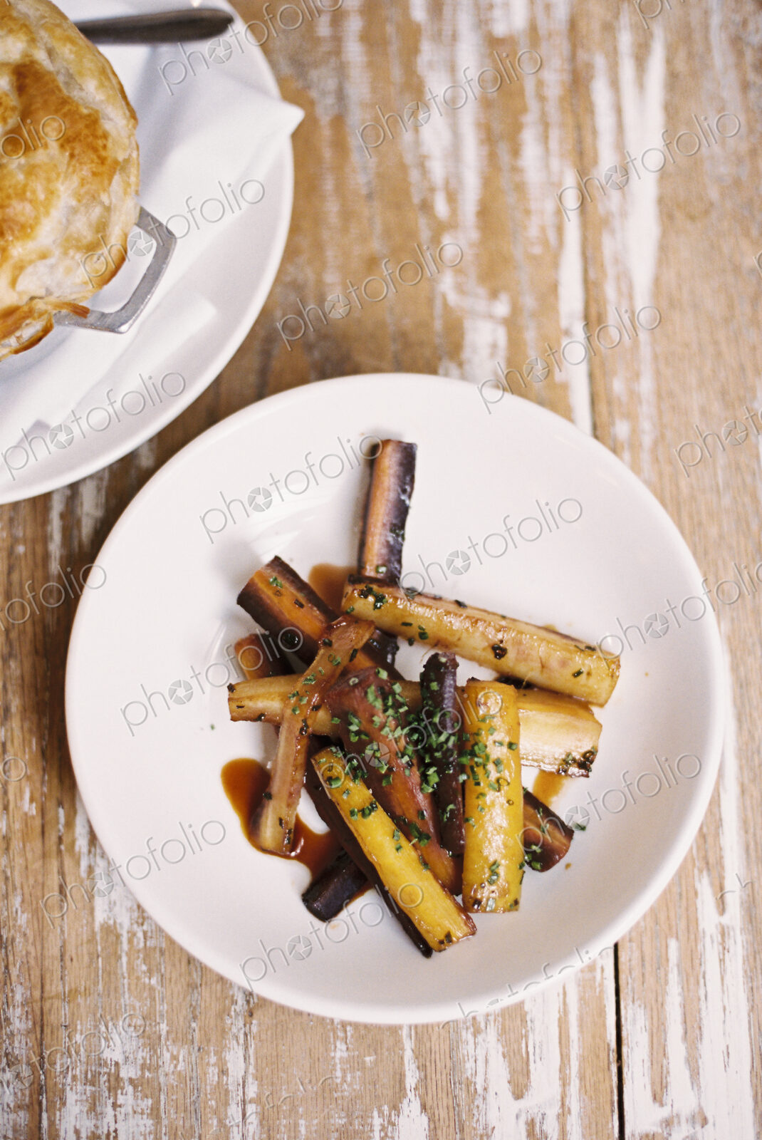A plate of roasted vegetables cut into batons, and a pie on a tabletop.