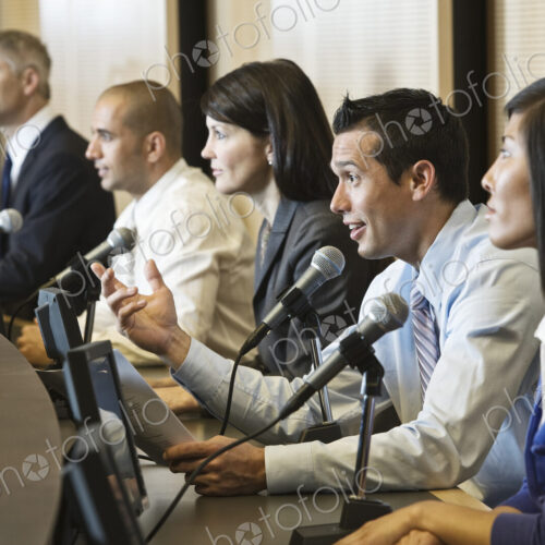 A political meeing with a mixed race group of people at microphones.