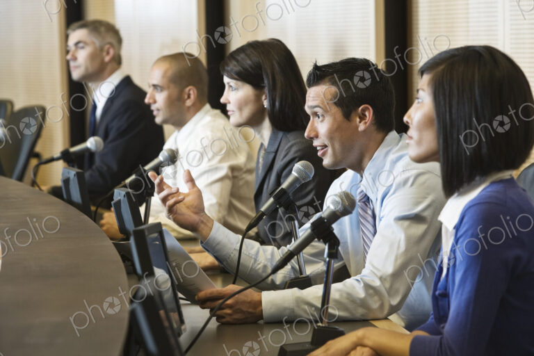 A political meeing with a mixed race group of people at microphones.