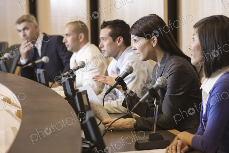 A political meeing with a mixed race group of people at microphones.