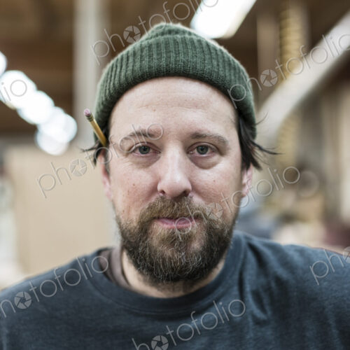 A portrait of a Caucasian carpenter working in a large woodworking shop.
