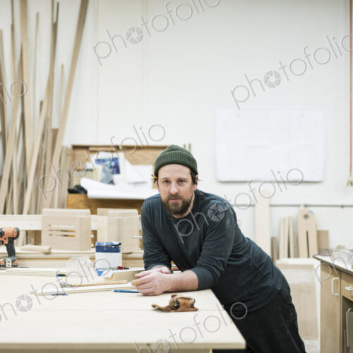 A portrait of a Caucasian carpenter working in a large woodworking shop.