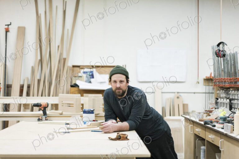A portrait of a Caucasian carpenter working in a large woodworking shop.