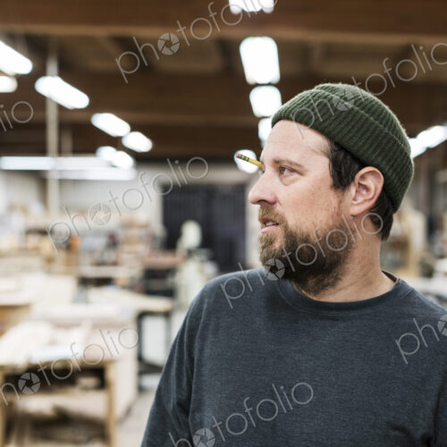 A portrait of a Caucasian carpenter working in a large woodworking shop.