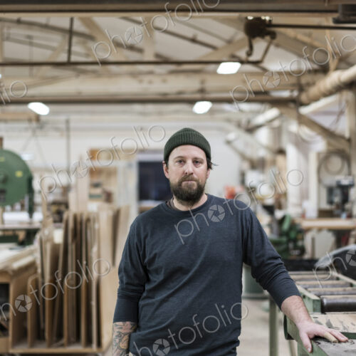 A portrait of a Caucasian carpenter working in a large woodworking shop.