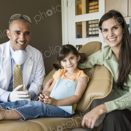 A portrait of a Middle Eastern male dentist a female child patient and her mom in a… A portrait of a Middle Eastern male dentist a female child patient and her mom in a…