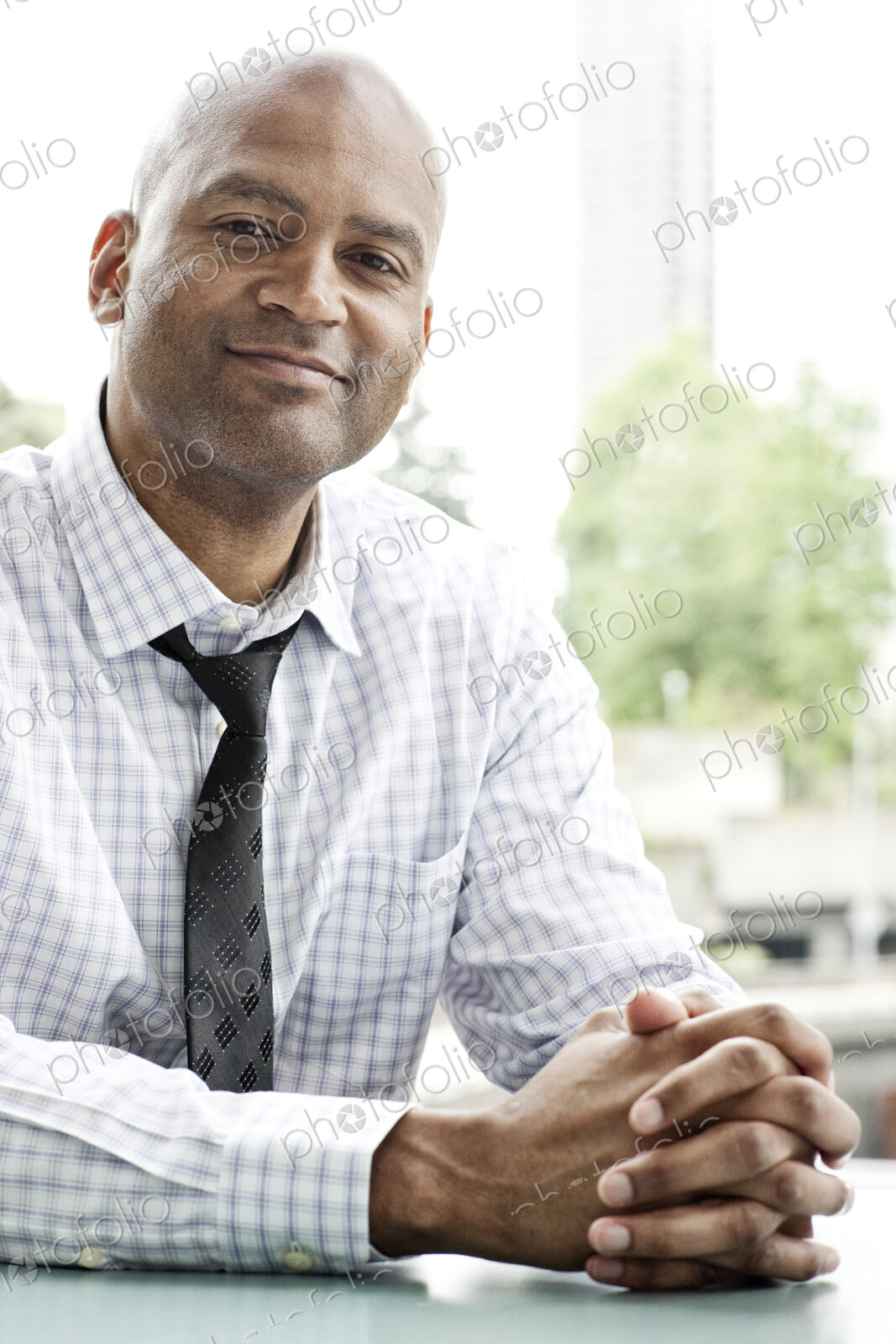 A portrait of a black businessman in a shirt and tie sitting at a desk next to a window.