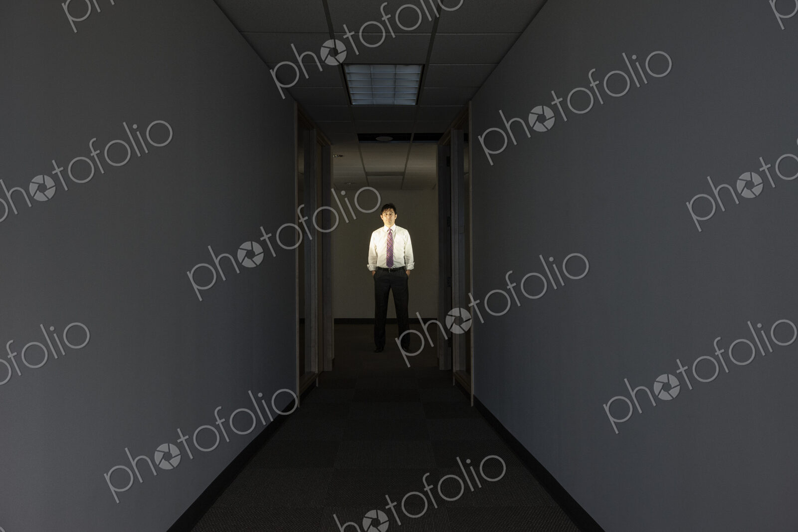 A portrait of a black businessman standing at the end of a long dark hallway.