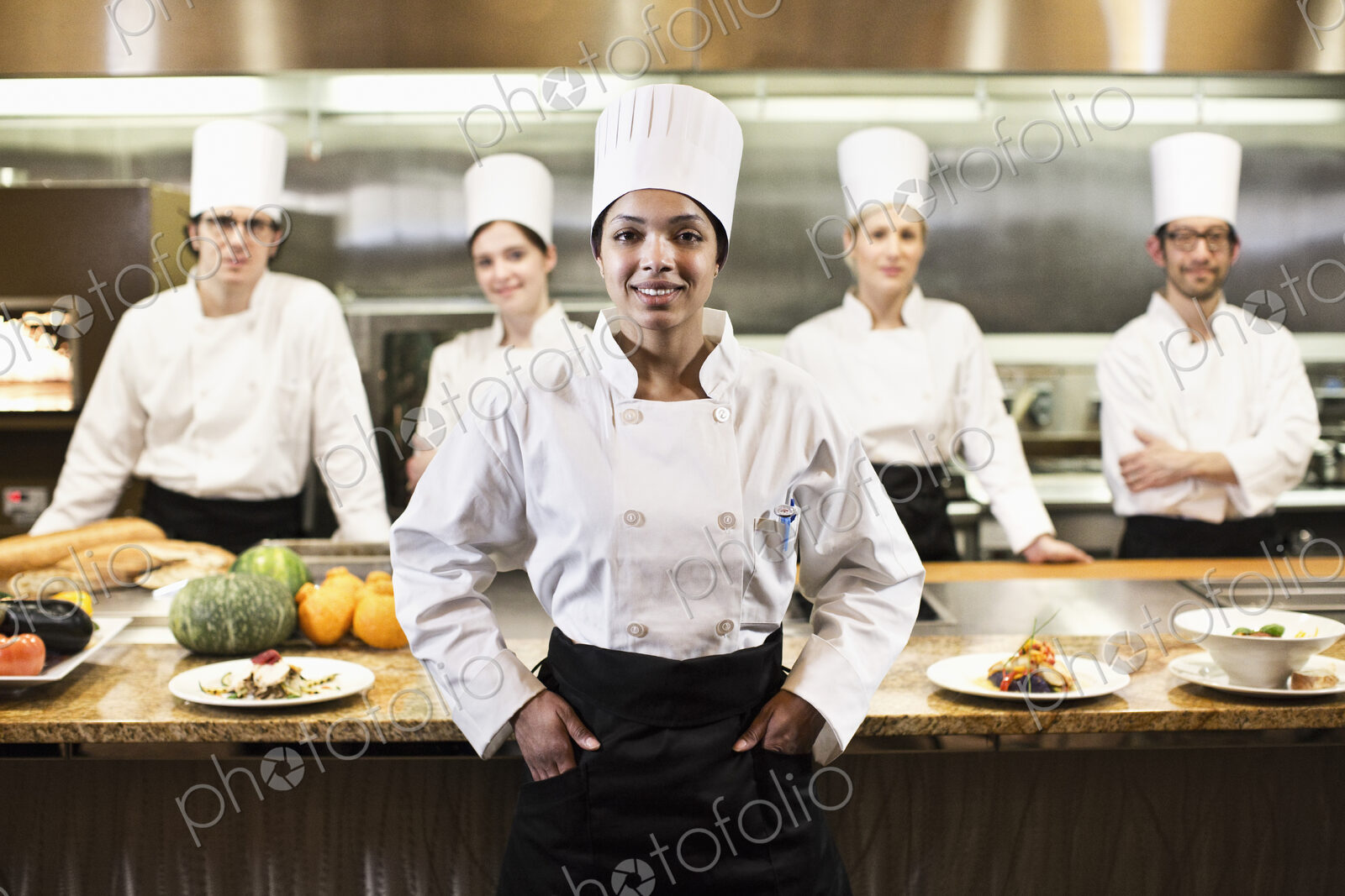 A portrait of a black female chef and her team of chefs in the backgroiund of a…