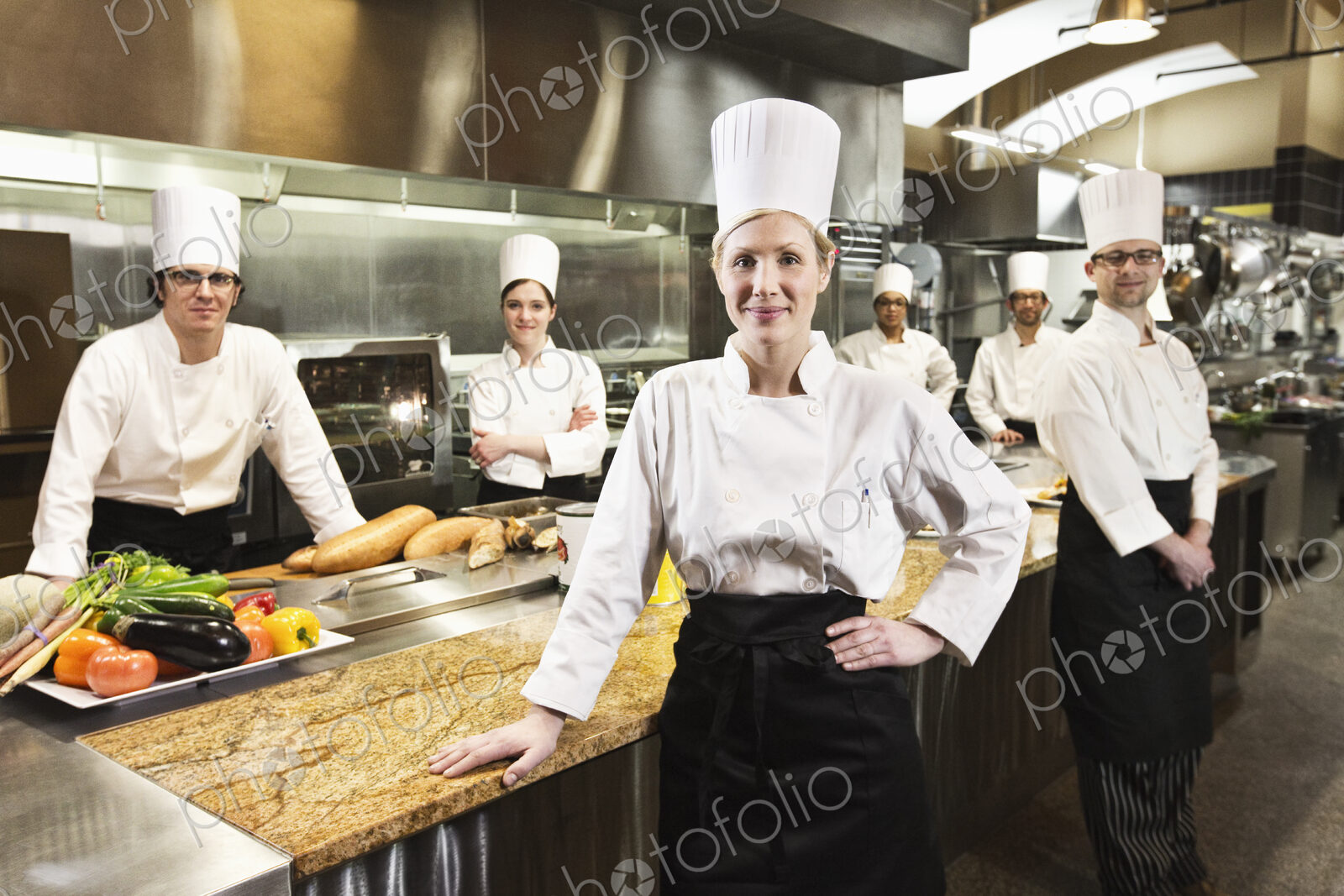 A portrait of a caucasian female chef and her team of chefs in the backgroiund.
