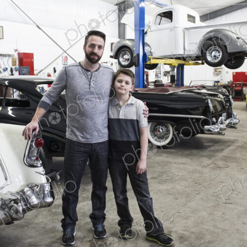 A portrait of a caucasian male and his young son in their classic car repair shop.