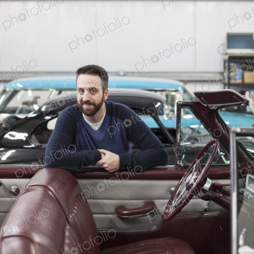 A portrait of a caucasian male leaving on the side of his classic car convertible in a…
