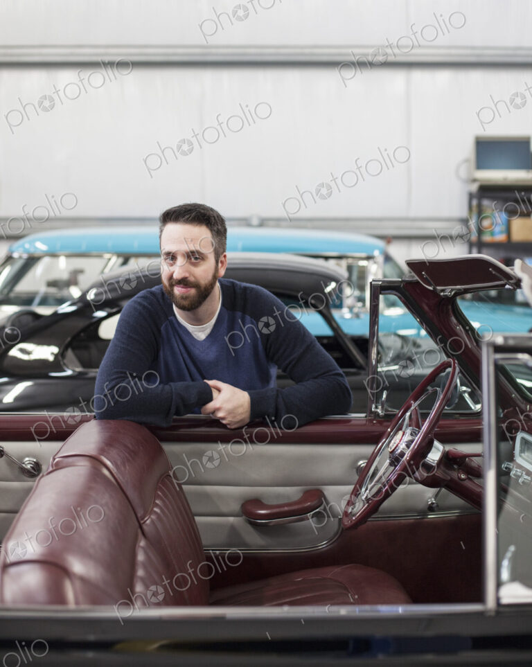 A portrait of a caucasian male leaving on the side of his classic car convertible in a…