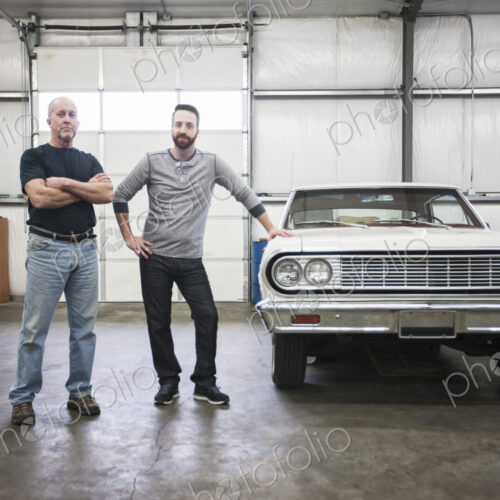 A portrait of a caucasian senior car mechanic and his son in their classic car repair…