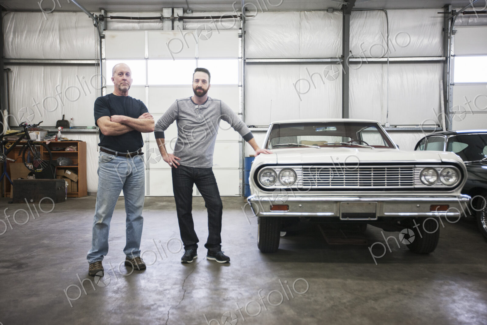 A portrait of a caucasian senior car mechanic and his son in their classic car repair…