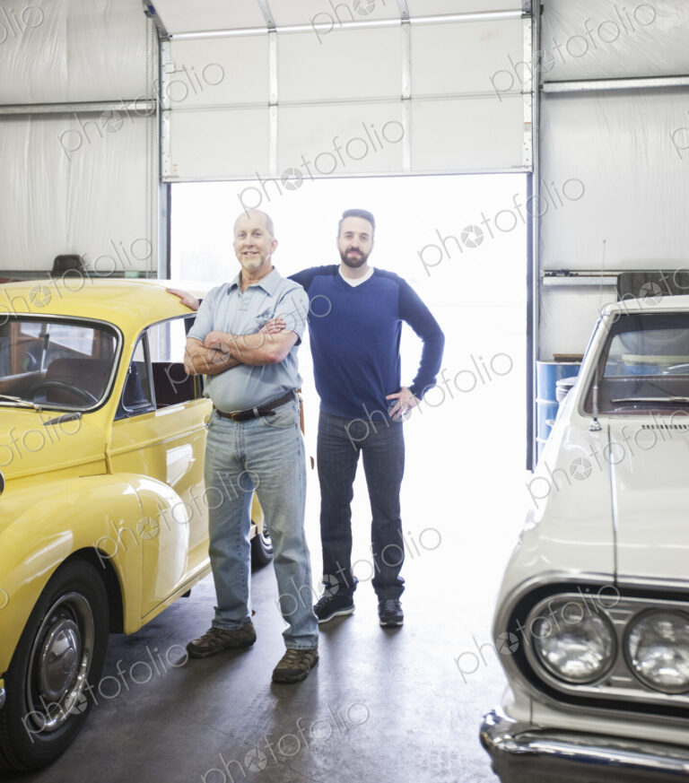 A portrait of a caucasian senior car mechanic and his son in their classic car repair…