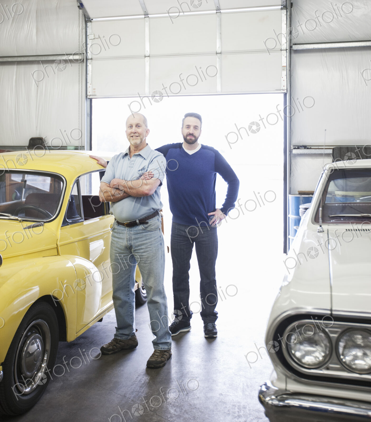 A portrait of a caucasian senior car mechanic and his son in their classic car repair…