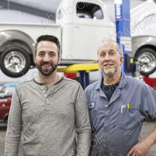 A portrait of a caucasian senior car mechanic and his son in their classic car repair…